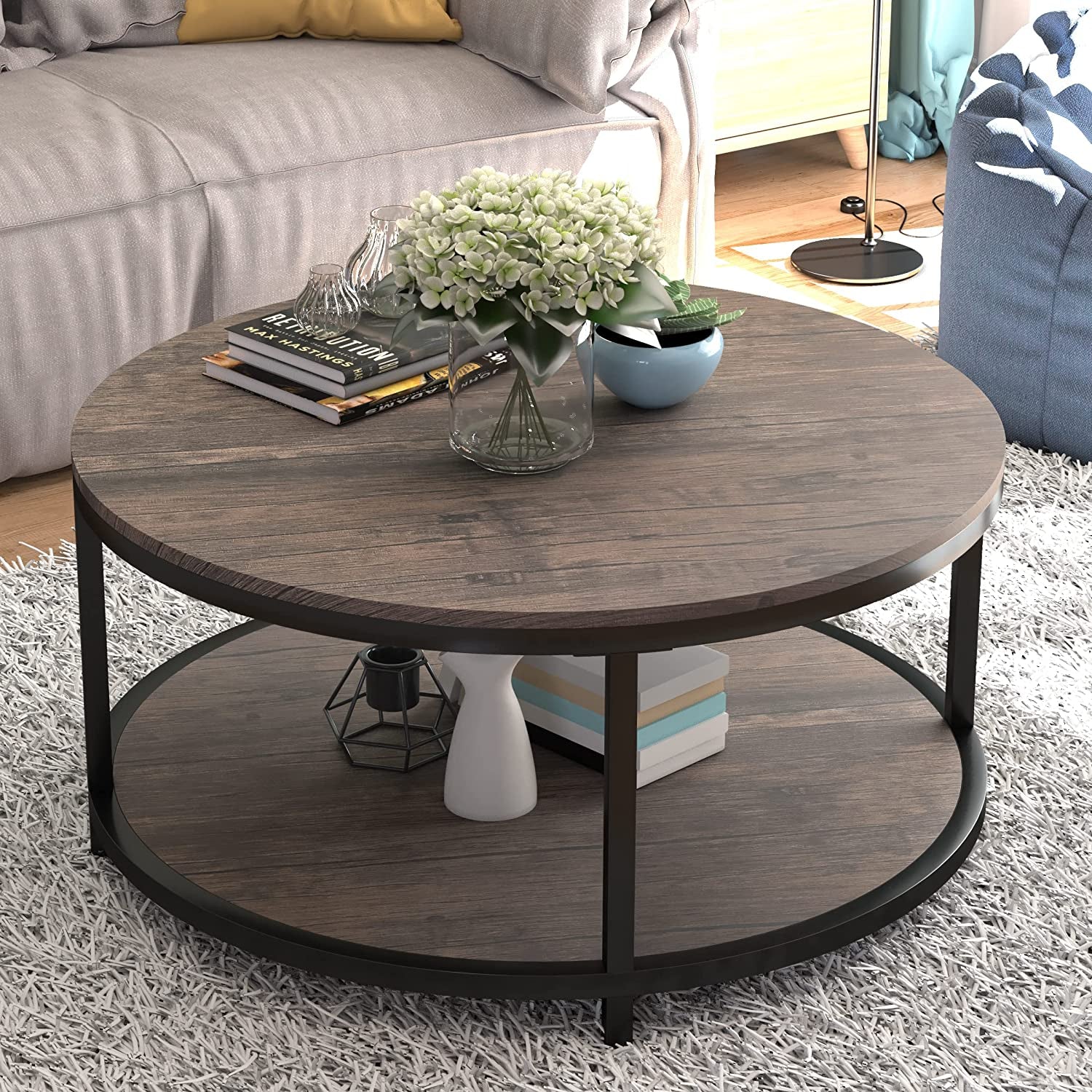 Round two-tier coffee table in light walnut finish shown angled with decorative books and vase on top