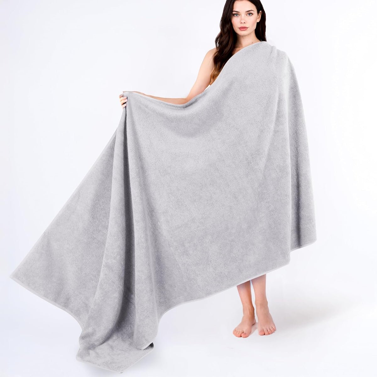 Woman holding a large light gray towel wrapped around her, towel spilling to the floor