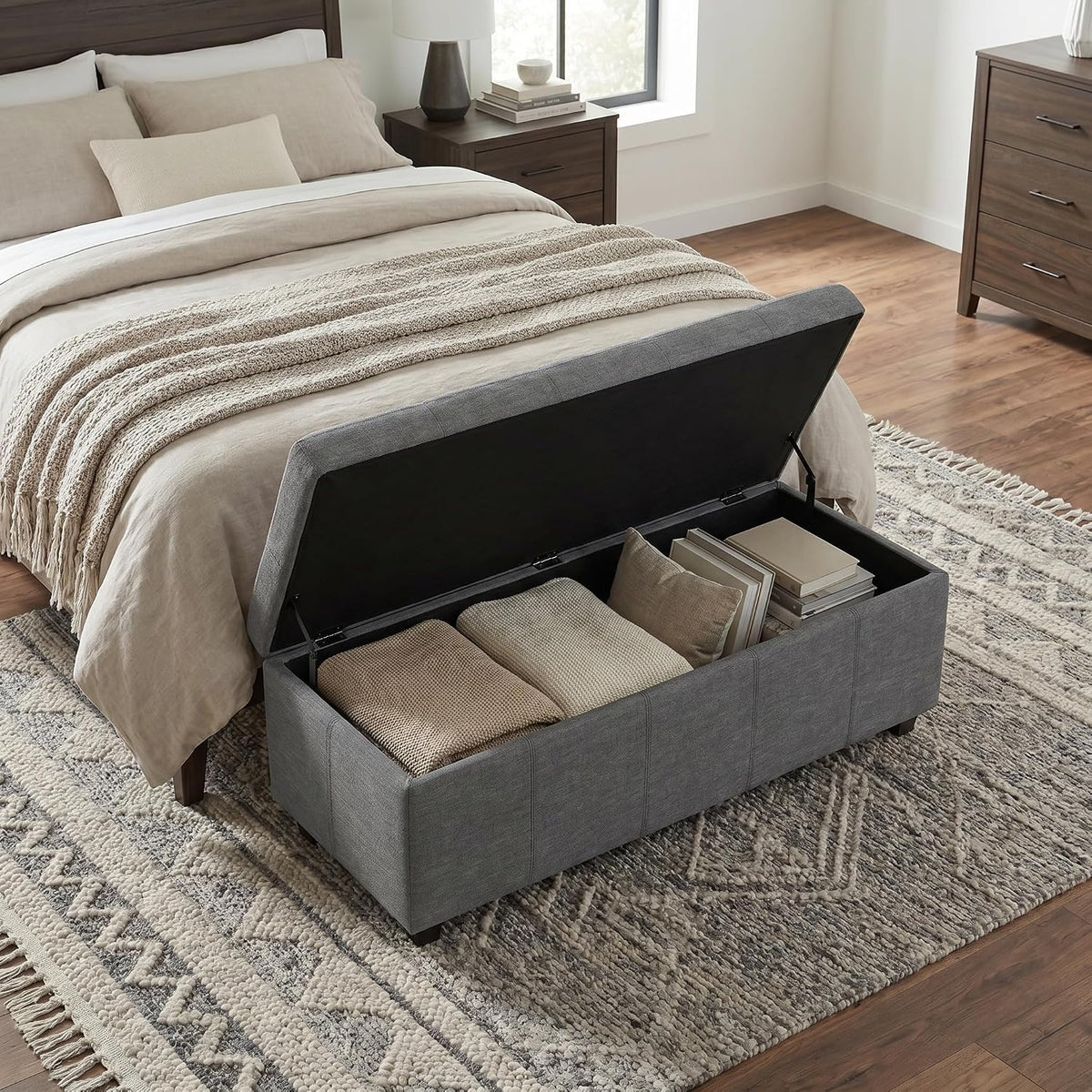 Open slate grey storage ottoman bench showing interior storage with folded blankets at foot of bed