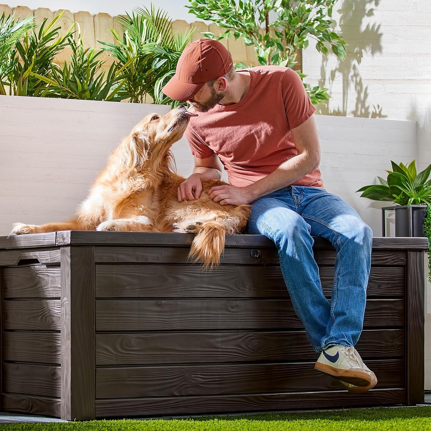 Brown resin deck box shown as bench with a man seated and a golden retriever lying on the closed lid