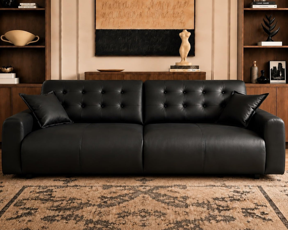 Straight-on view of a three-seat tufted leather sofa with two throw pillows against a styled wall.