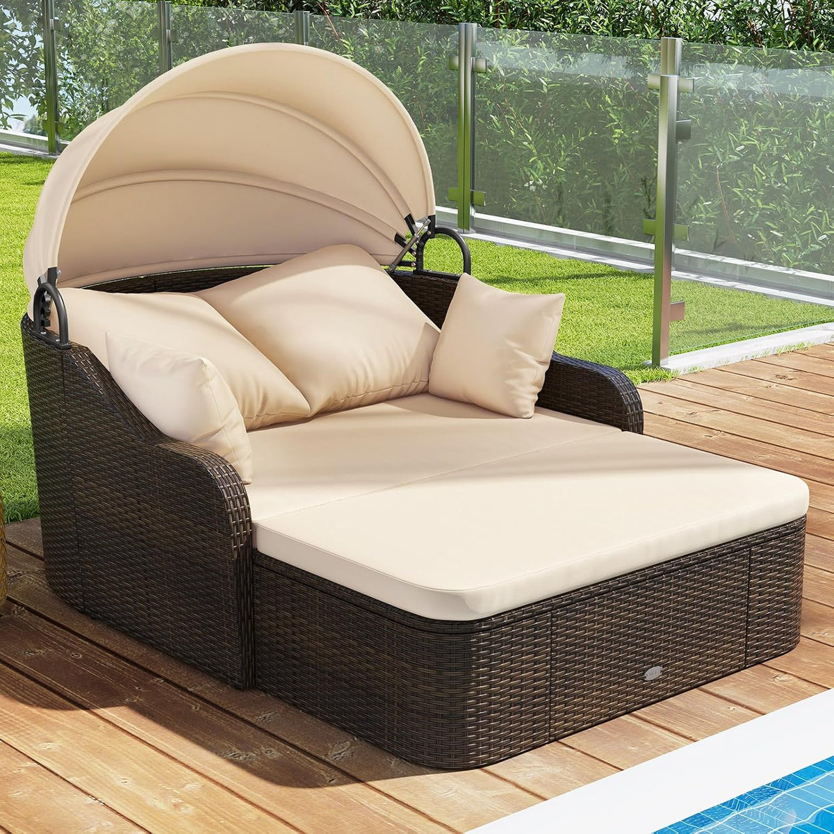 Brown woven rattan daybed with raised beige canopy and cushions on a wood deck beside a pool