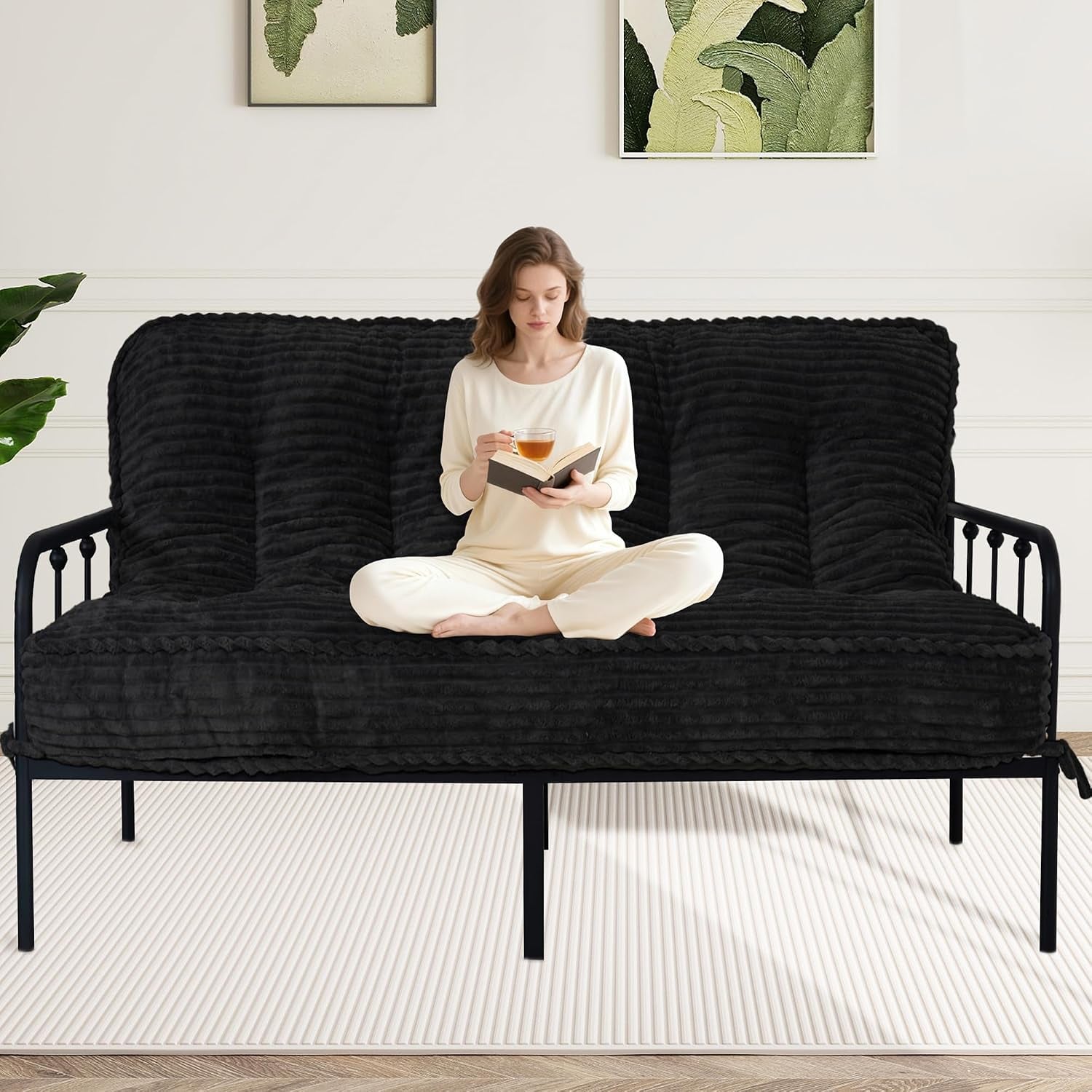 Woman reading with tea on a ribbed black futon mattress on a black metal frame in a neutral room