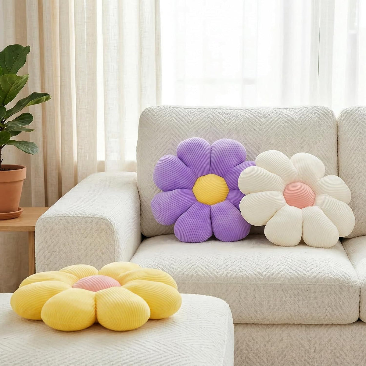 Purple and cream daisy pillows on a sofa with a yellow daisy cushion visible on a nearby ottoman, lifestyle scene