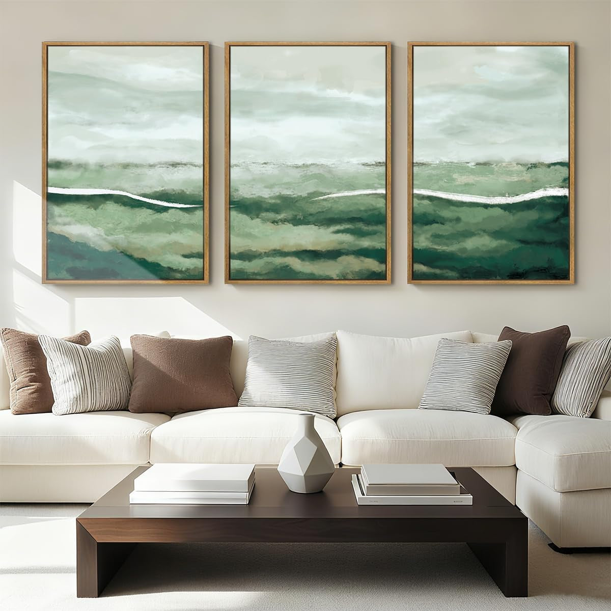 Triptych of green abstract seascape prints in thin wood frames over a cream sectional sofa and low dark coffee table.
