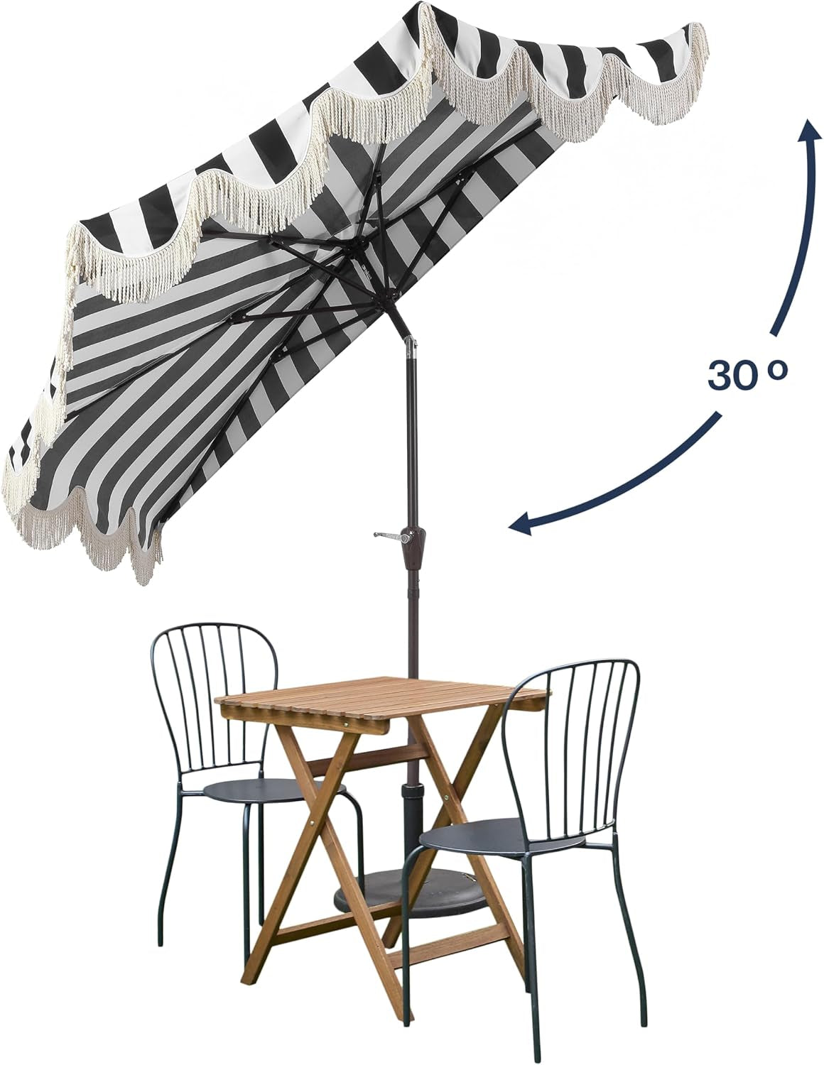 Angled lifestyle shot of umbrella tilted over a small patio table and two metal chairs, showing scalloped fringe.