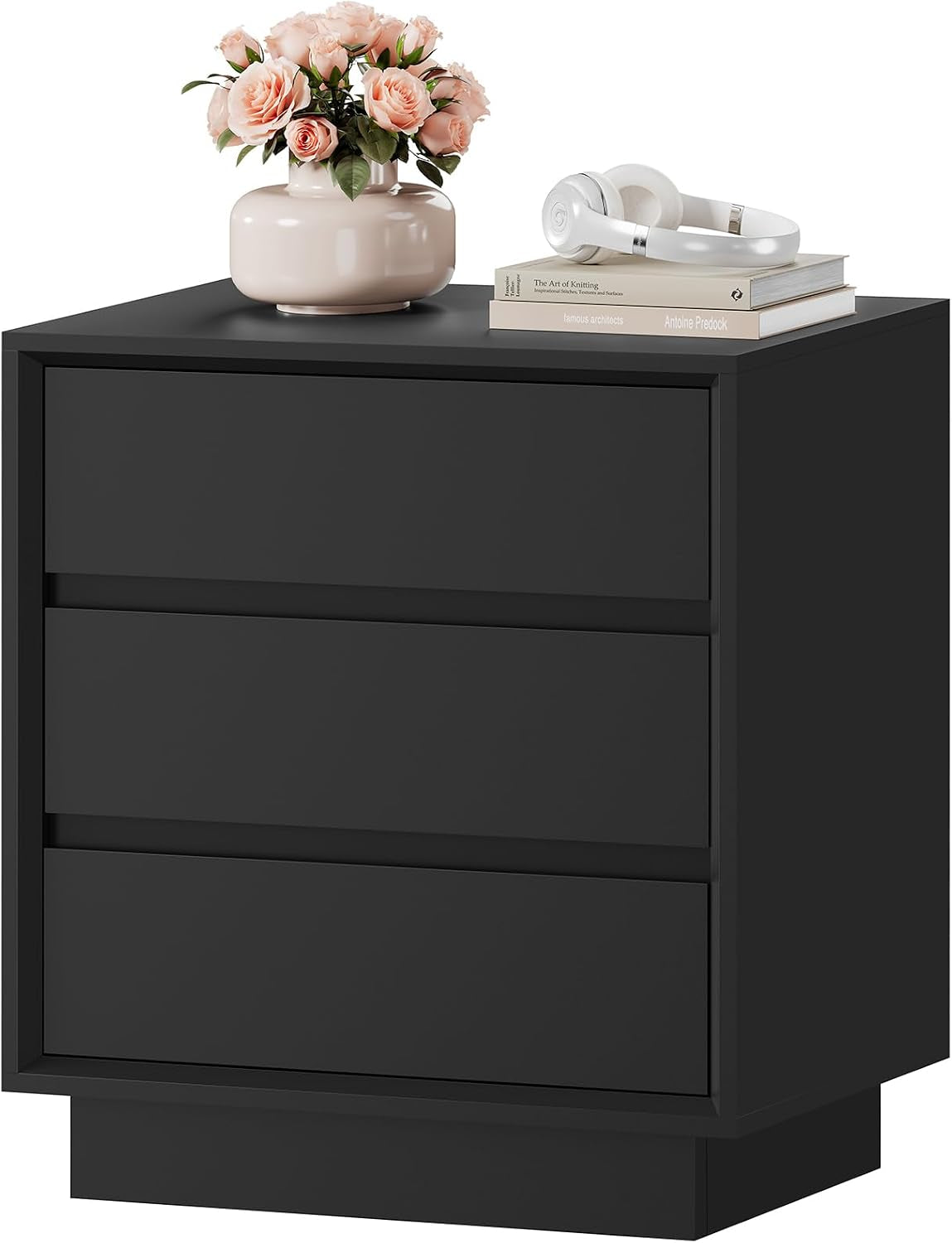 Black three-drawer nightstand with squared edges and pedestal base, vase and headphones on top.