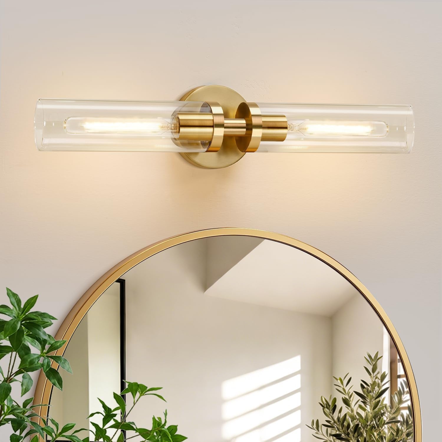 Single horizontal brushed-gold sconce mounted above a round mirror with plants below.