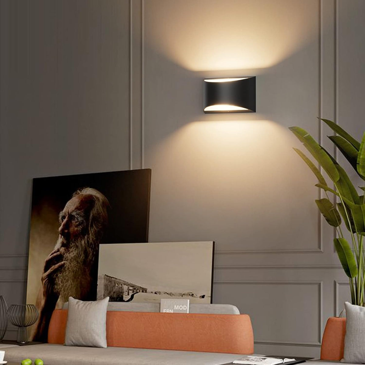 Close view of a single black curved wall sconce illuminating a paneled wall above a sofa and plants.