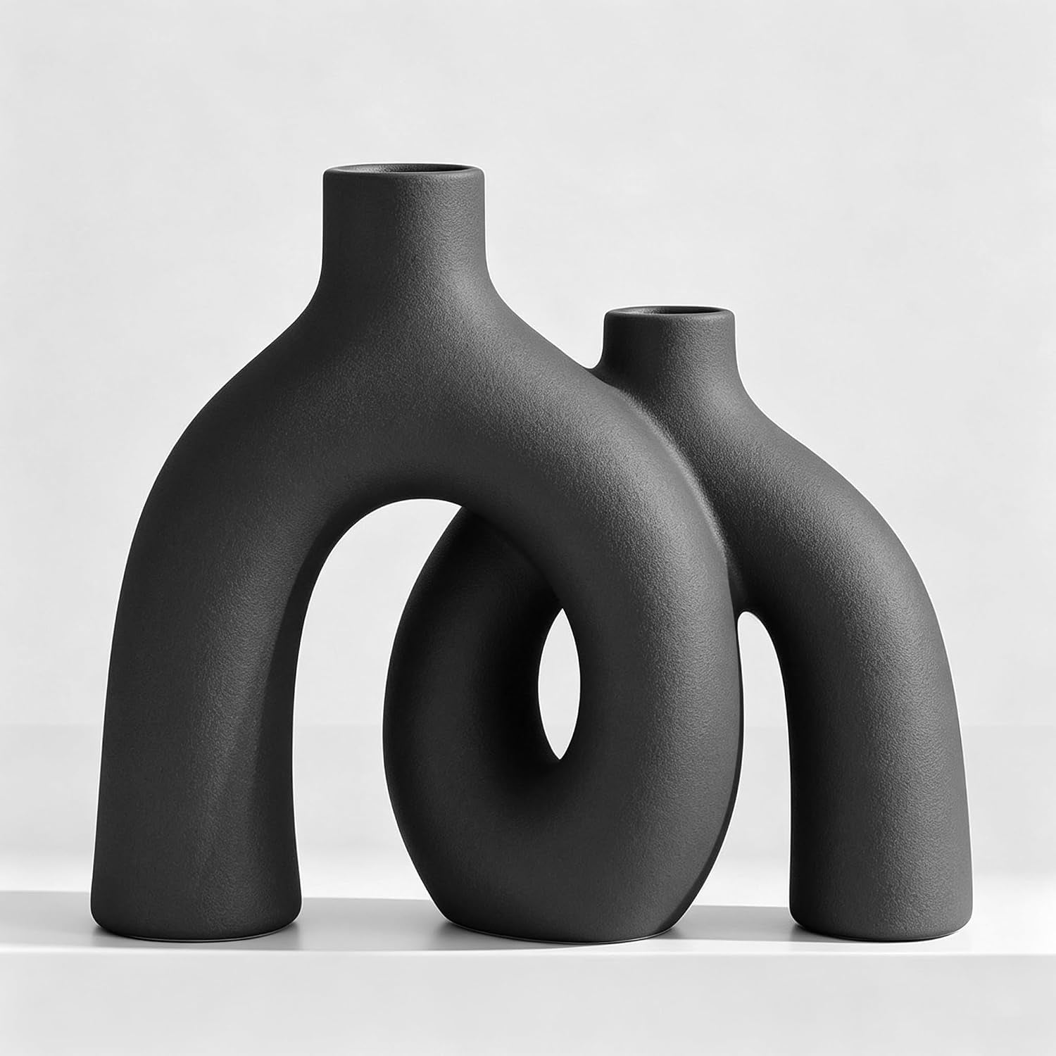 Two intertwined donut vases in a deep charcoal gray with textured finish