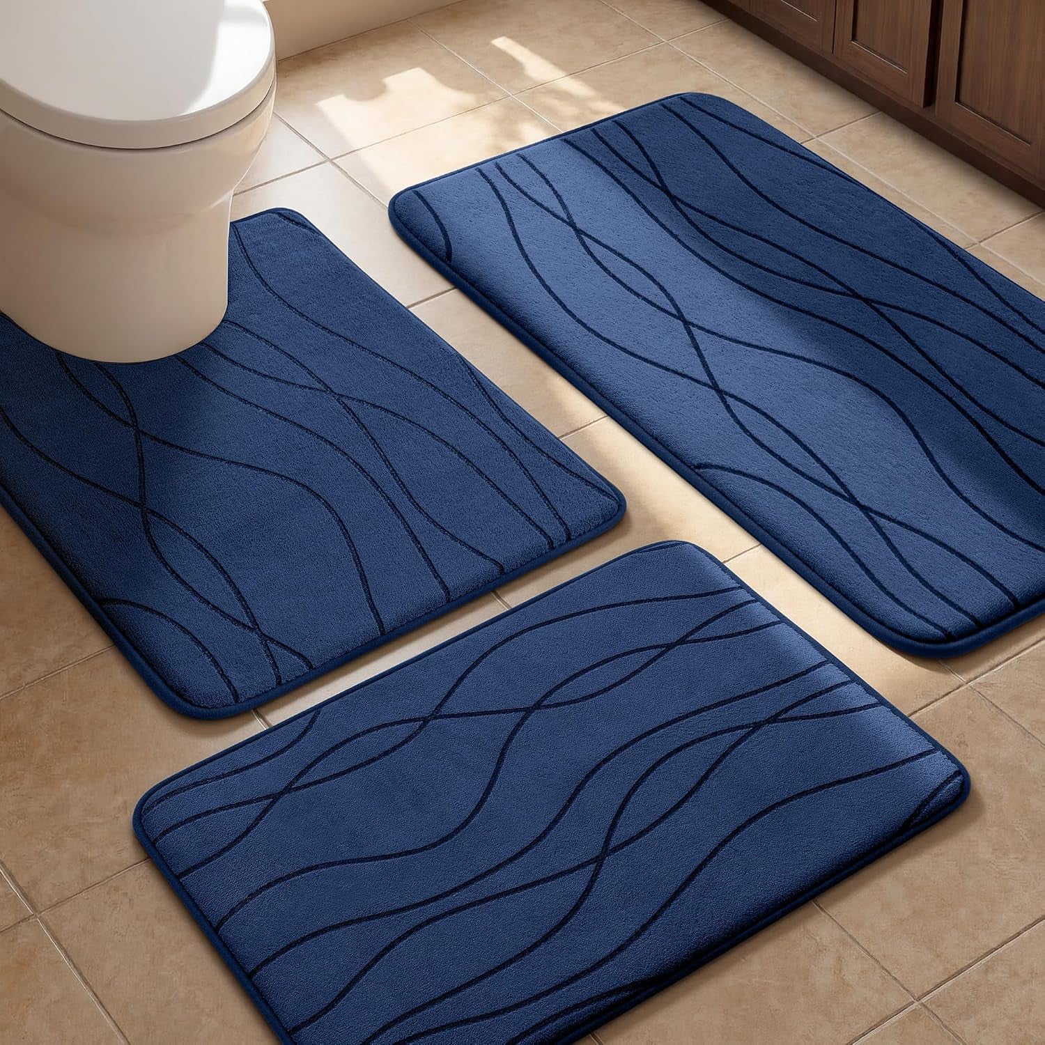 Three navy blue bathroom rugs placed on tile around a toilet, close angled view showing textured wave lines.