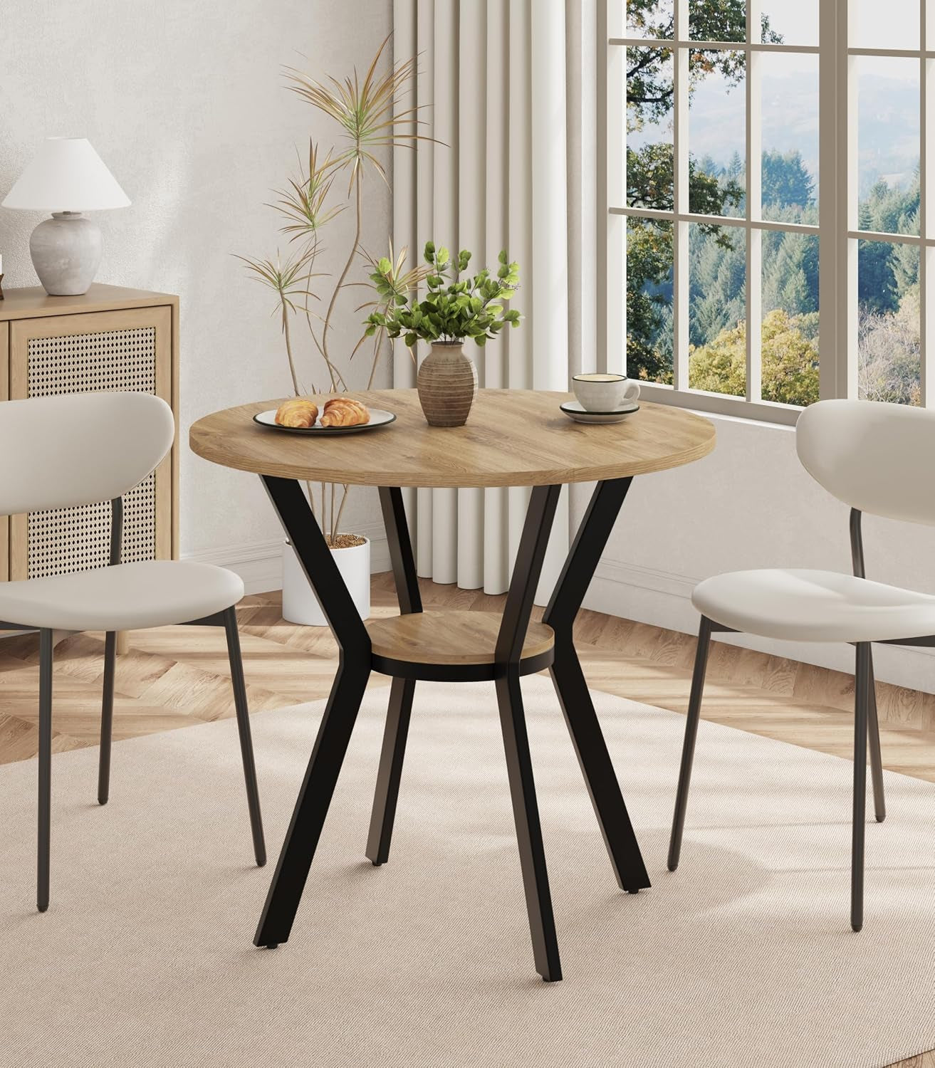 Round dining table with warm oak-look top, black metal angled legs and matching lower shelf in a sunlit dining nook.