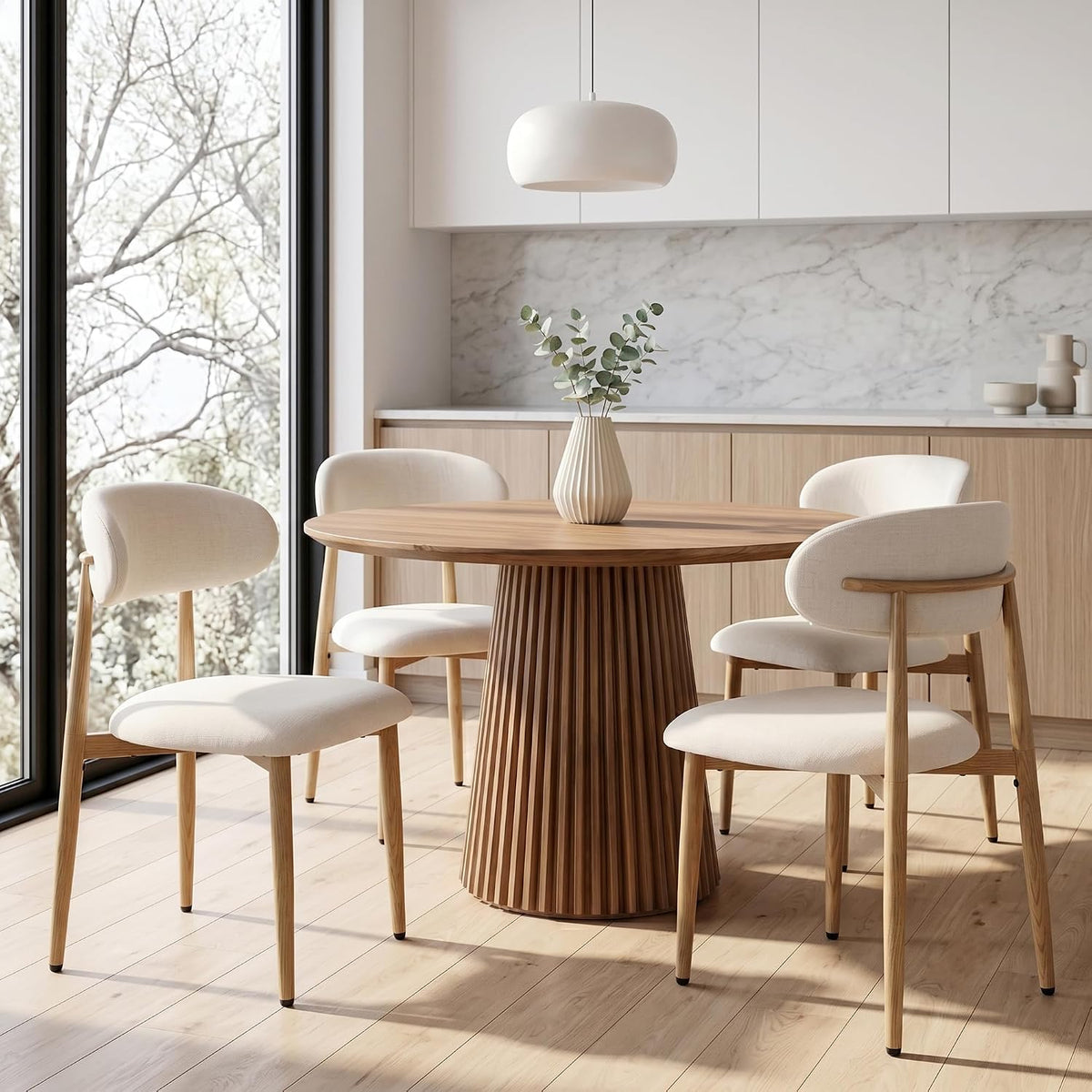 Beige upholstered dining chairs around a round wood table by a large window in a bright kitchen