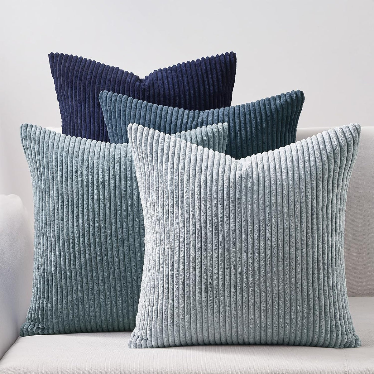 Four ribbed corduroy square pillows in varying blue tones arranged on a white couch.