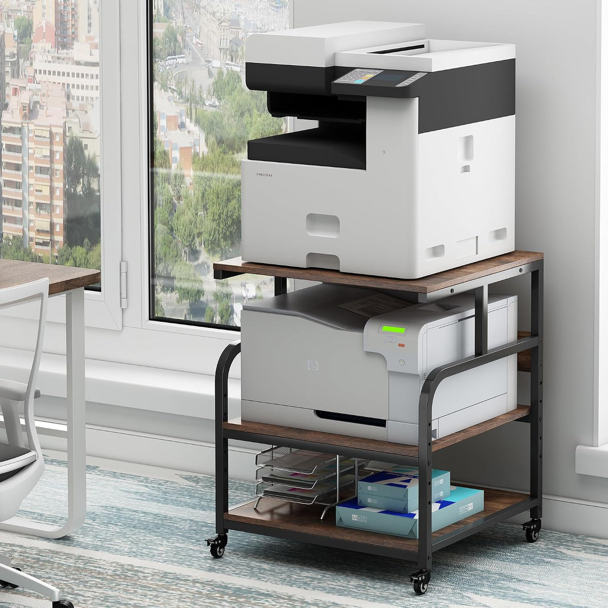 Black-framed 3-tier stand with wood-tone shelves by a window holding a large copier, paper, and trays.