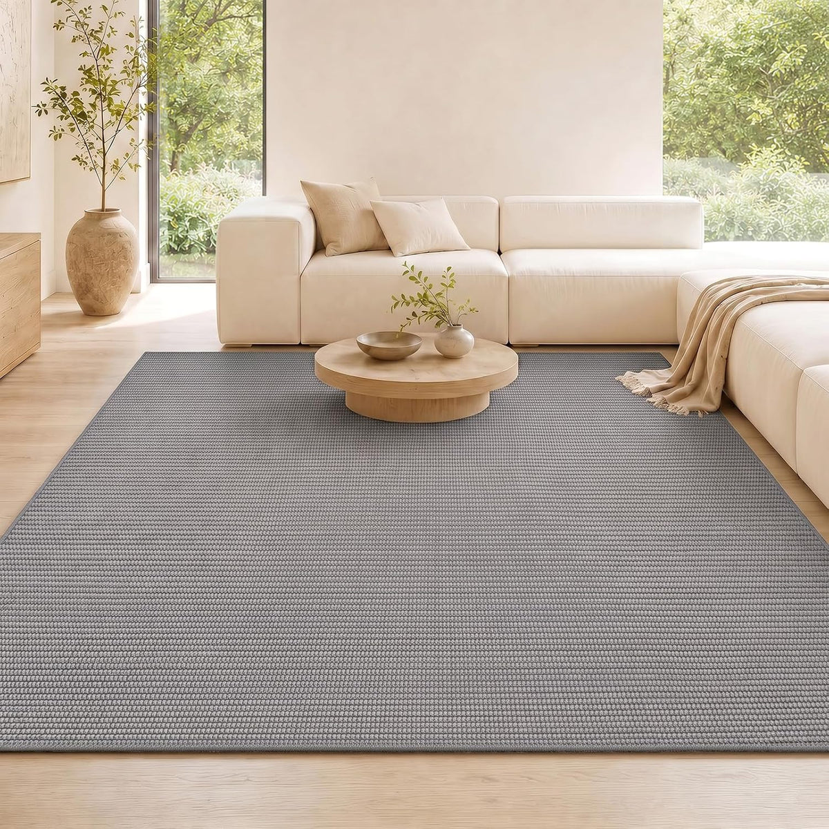 Grey rug anchoring a bright living room with a cream modular sofa and low round wooden coffee table.