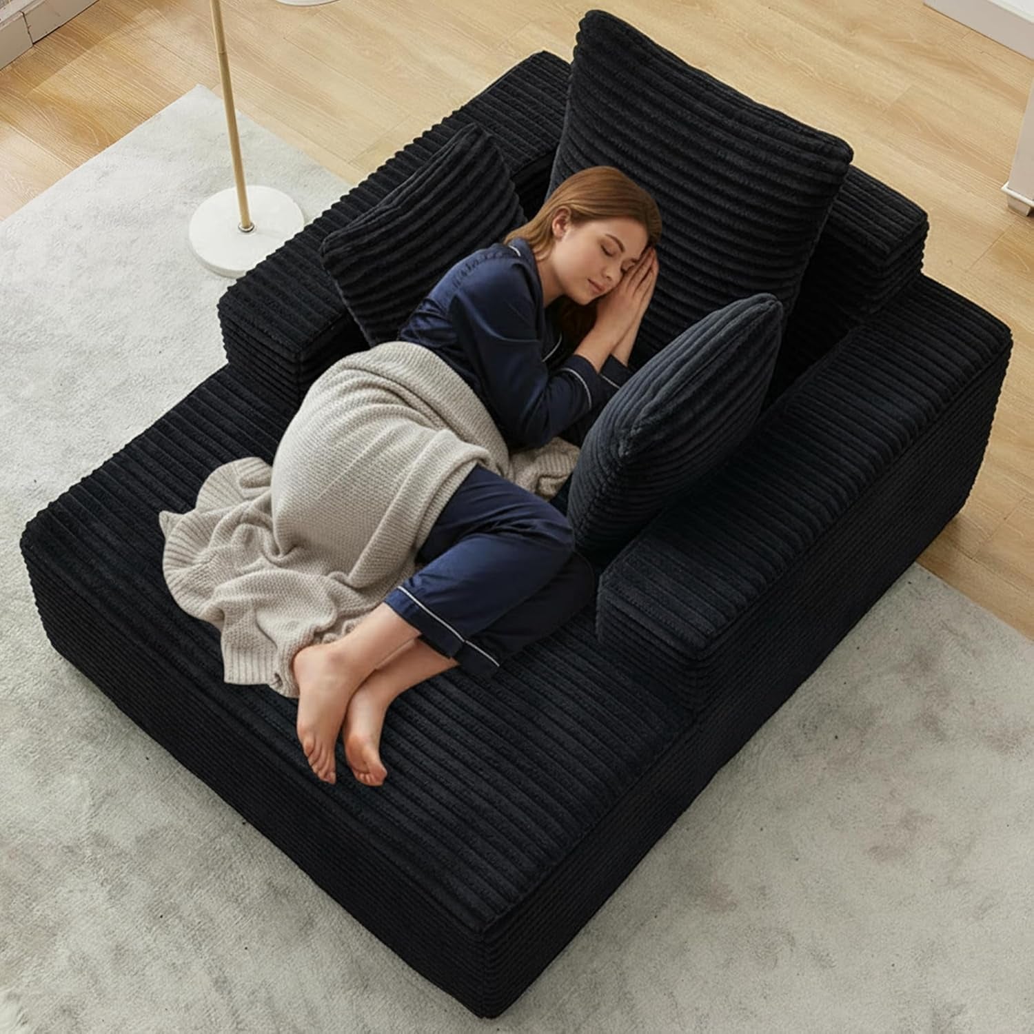 Black corduroy boneless chaise lounge with throw pillows shown from above with person lying down