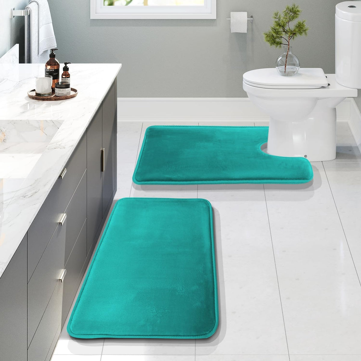 Bathroom view showing three teal memory-foam bath mats placed on a light tile floor beside a vanity and toilet.
