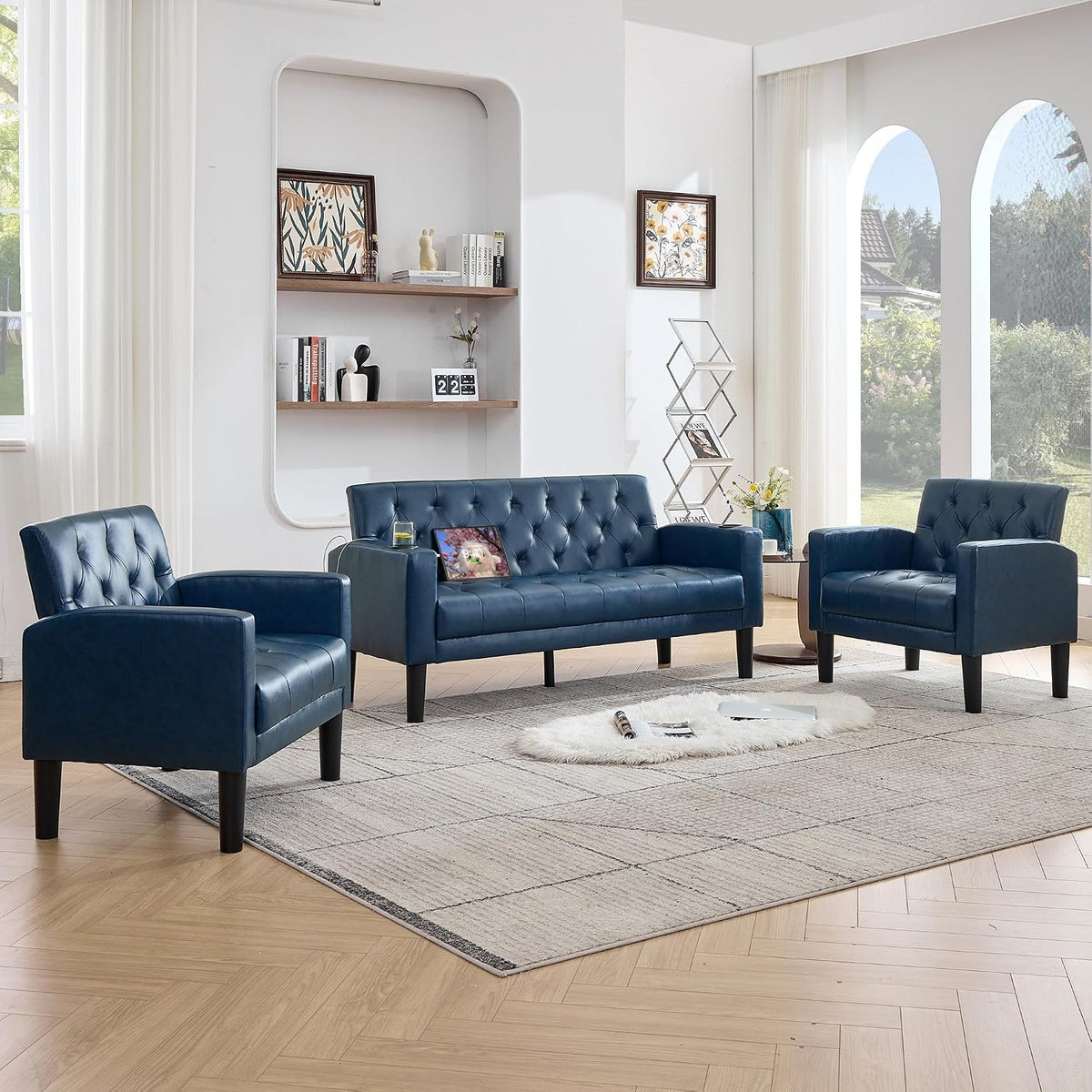 Wide frontal view of a blue tufted loveseat flanked by two matching armchairs in a sunlit living room.