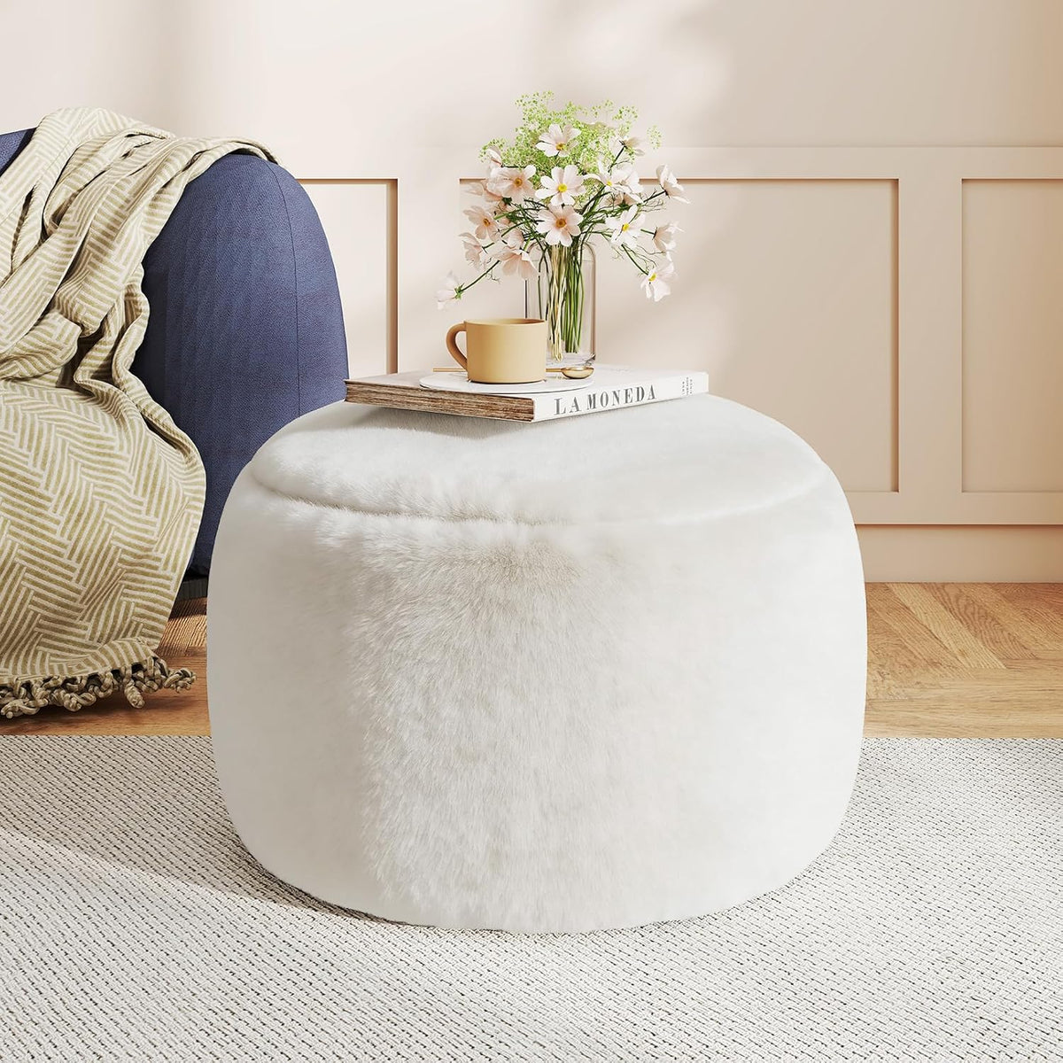 White faux fur pouf used as a small table with a book and vase next to a blue sofa