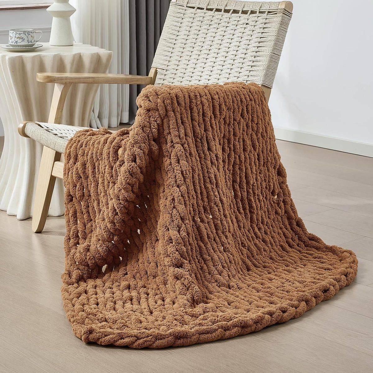 Deep brown chunky knit throw folded over the seat of a woven chair beside a side table