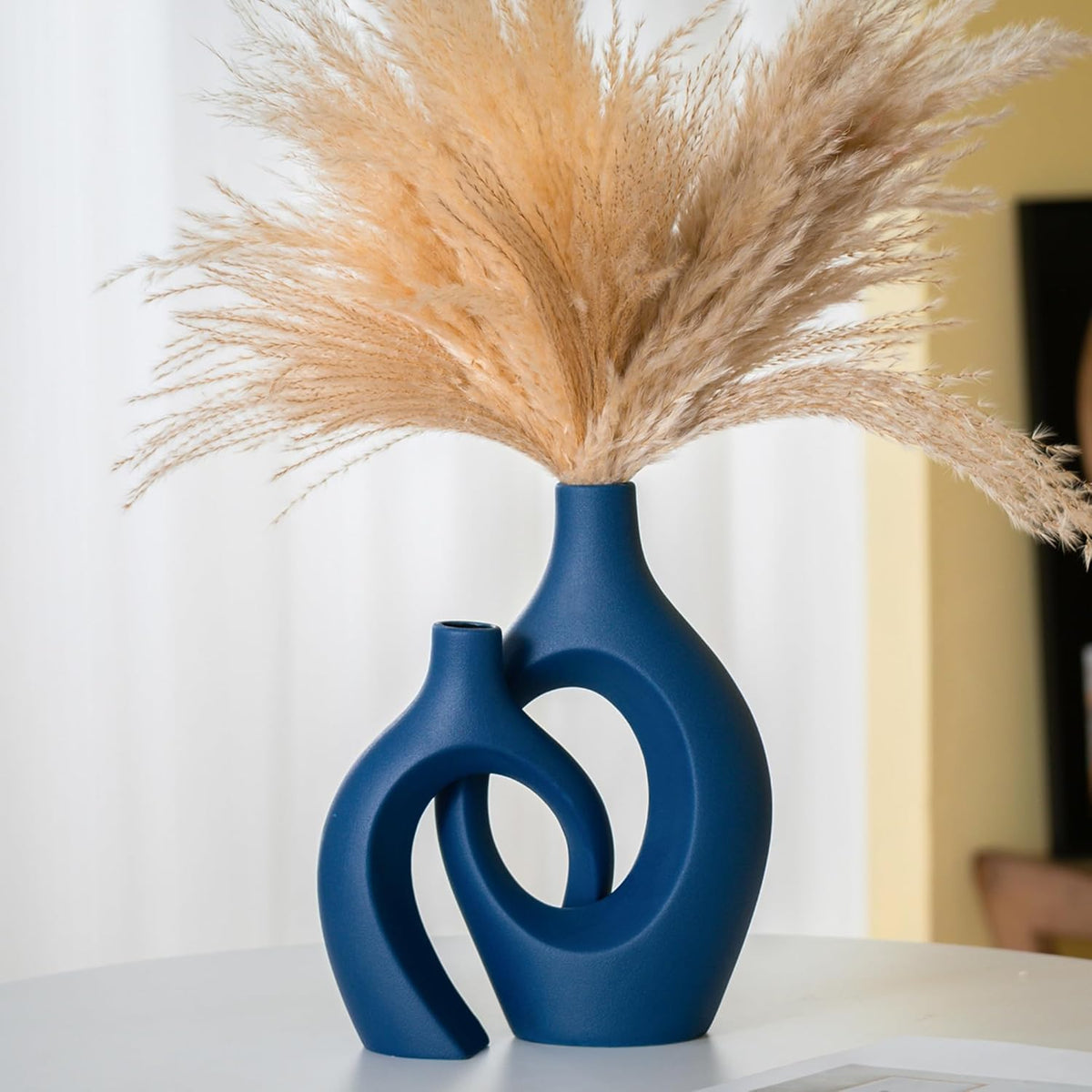 Front view of two blue hollow ceramic vases on a table holding a full spray of pampas grass.