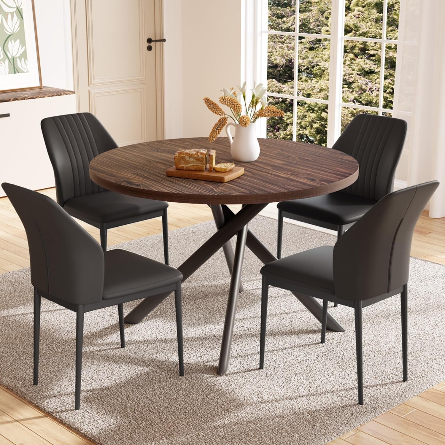 Dark-walnut round table with four black U-shaped chairs arranged on a rug by a window.