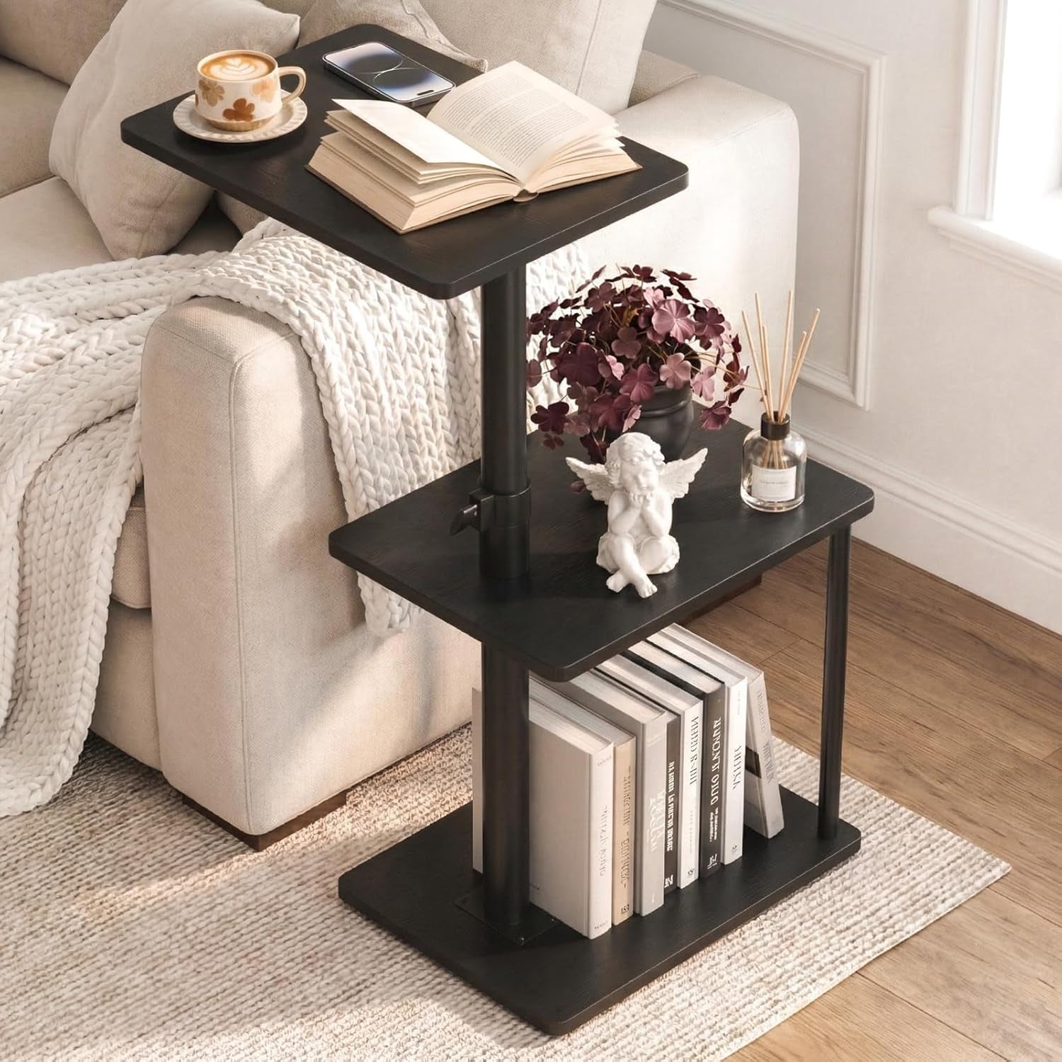 C-shaped three-tier side table in dark finish beside a light sofa with books and decor on shelves.