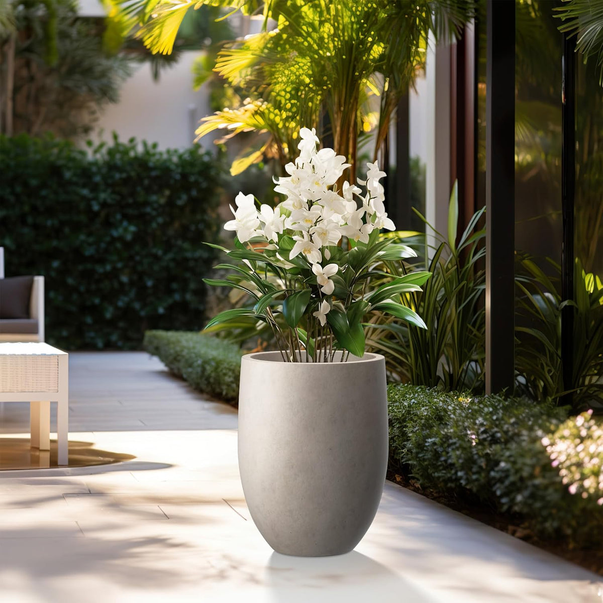 Outdoor patio scene with tall concrete planter in weathered finish holding white orchids