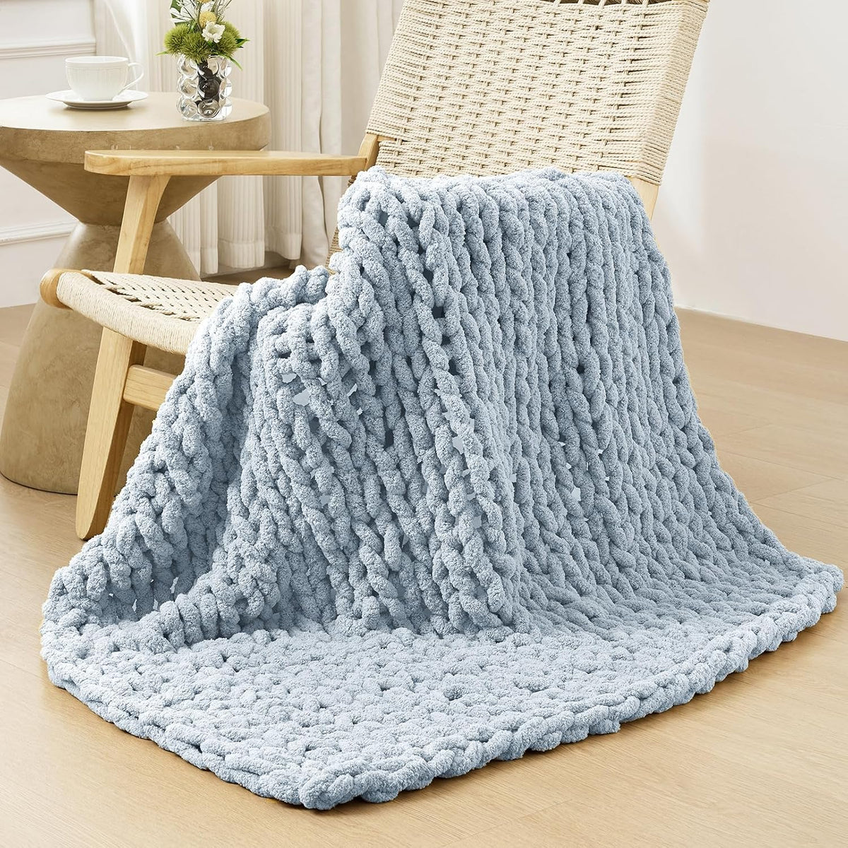 Light blue chunky knit blanket casually draped over a woven chair and spilling onto the floor.