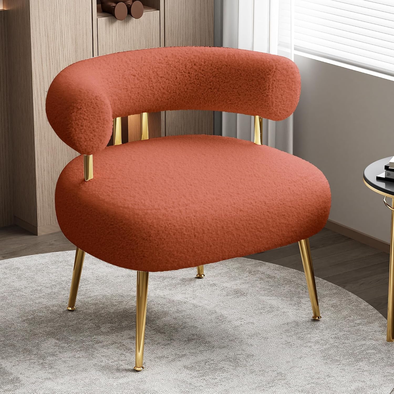 Rust-colored sherpa barrel chair with gold metal legs positioned on a circular rug in a light-filled room.