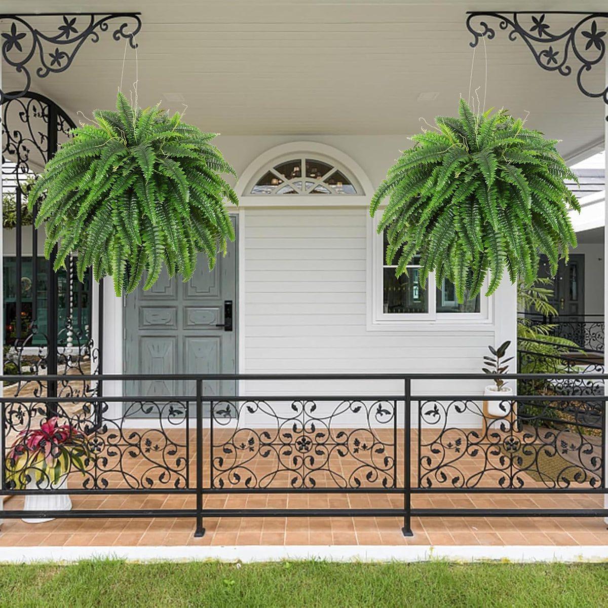 Pair of hanging green artificial Boston fern bushes under a covered porch with decorative railing