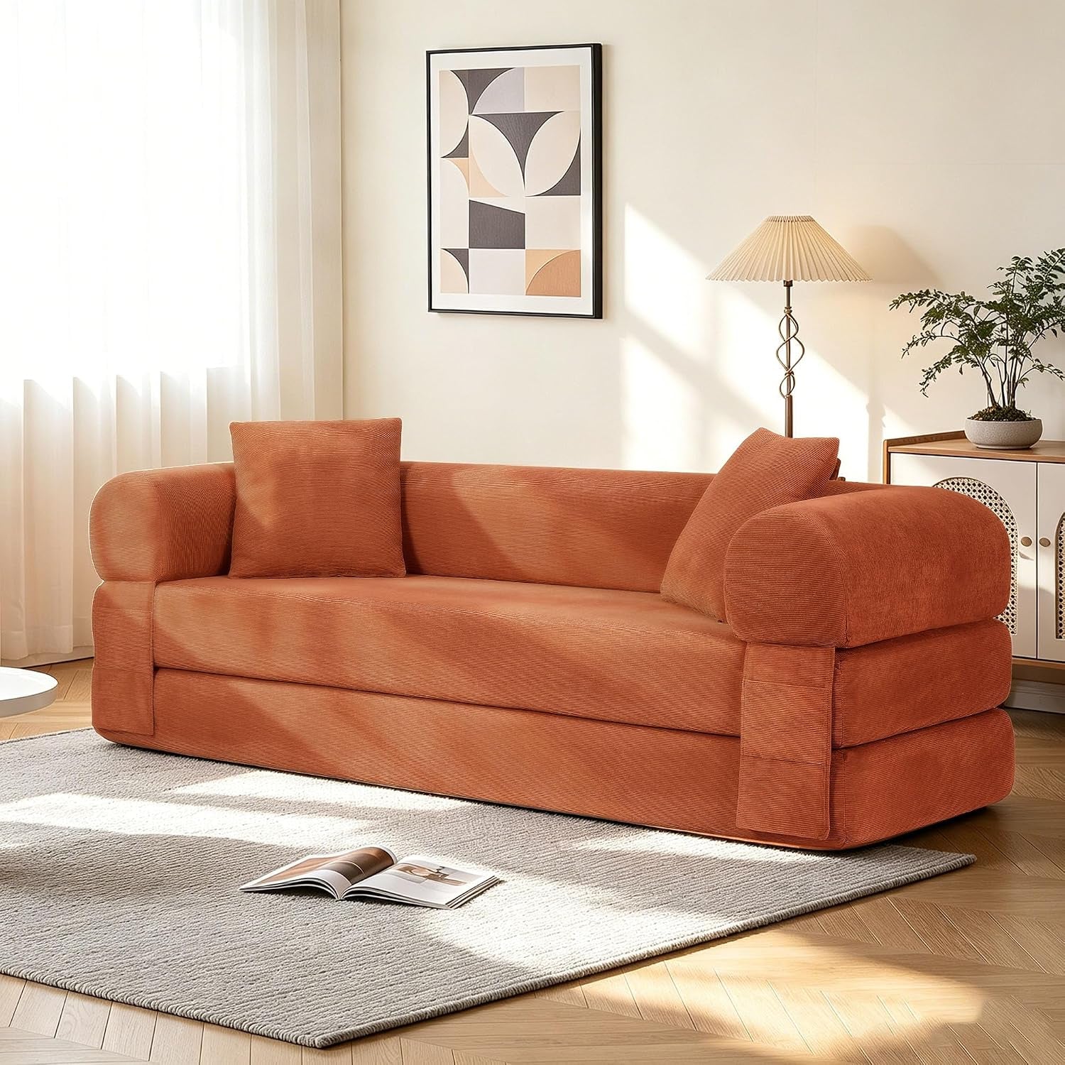 Angled view of a terracotta corduroy sofa with two pillows, rug, floor lamp, and framed art