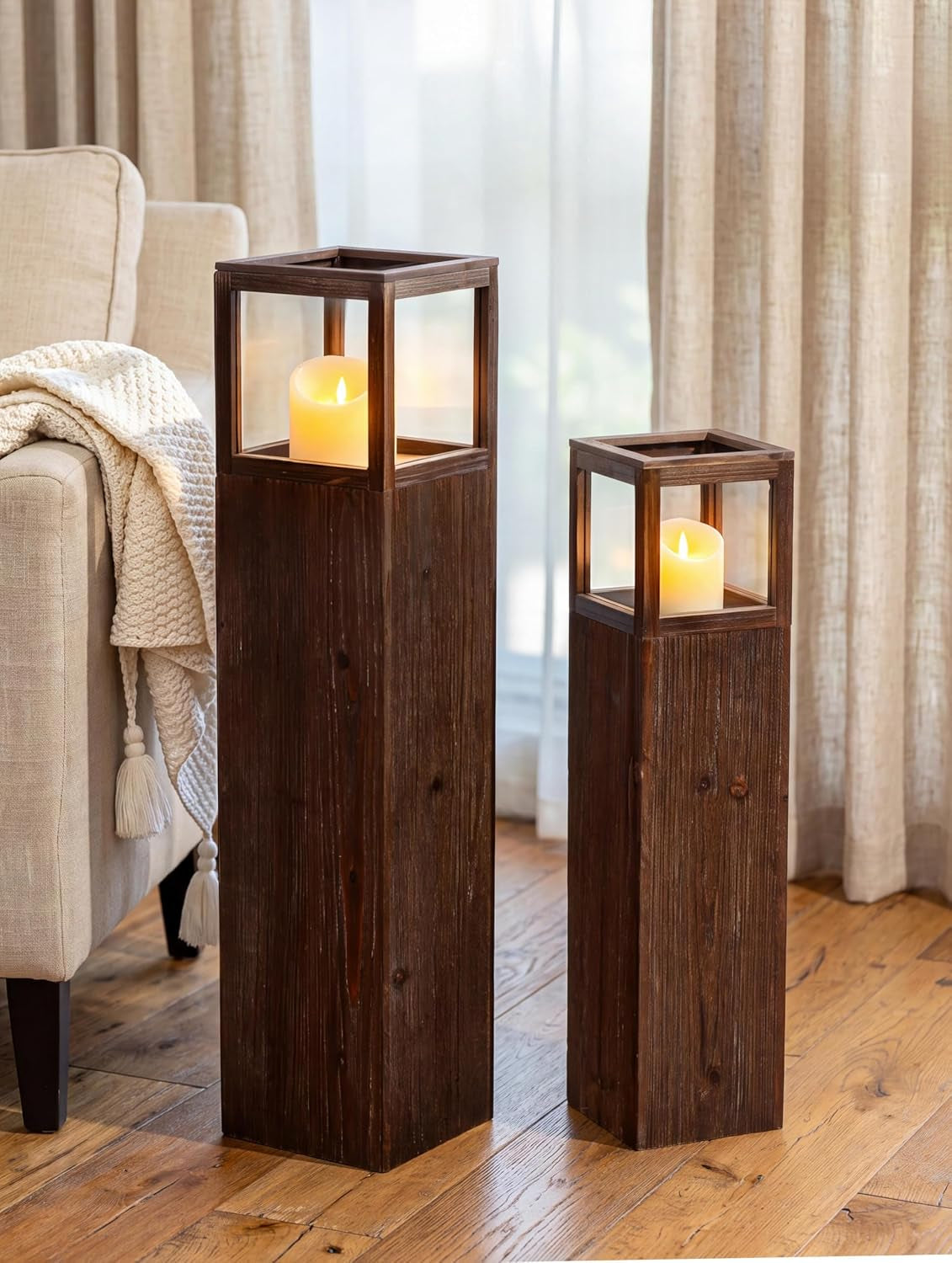 Distressed dark fir floor lantern pair with LED pillar candles, angled front view beside a sofa