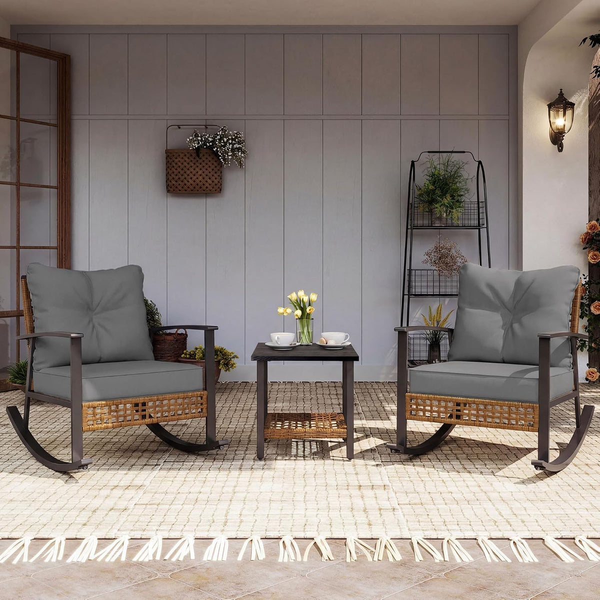 Patio scene with two gray-cushioned rocking chairs flanking a small two-tier coffee table with yellow tulips.