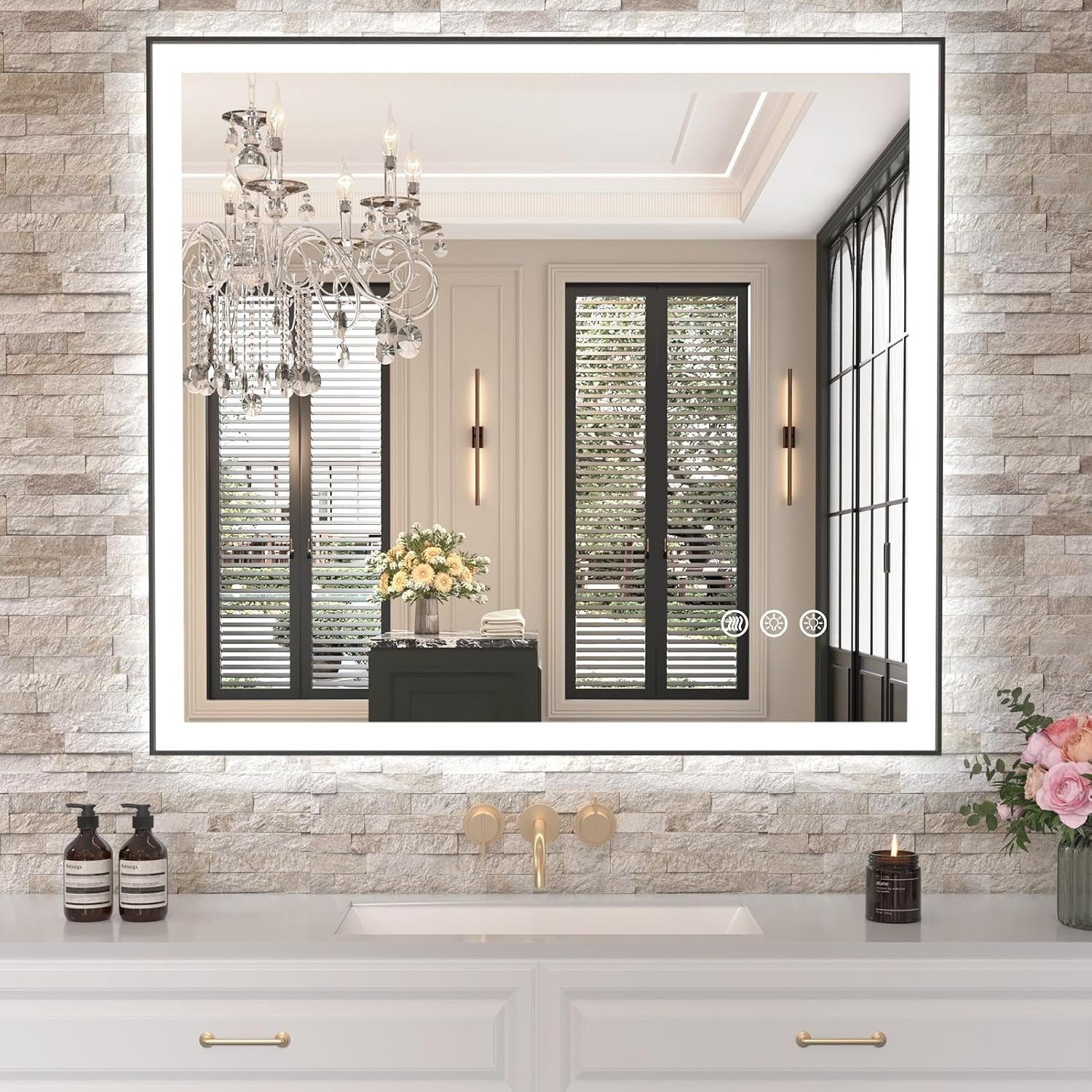 Front view of a lit rectangular mirror set in a stone-tiled wall reflecting chandelier and window shutters