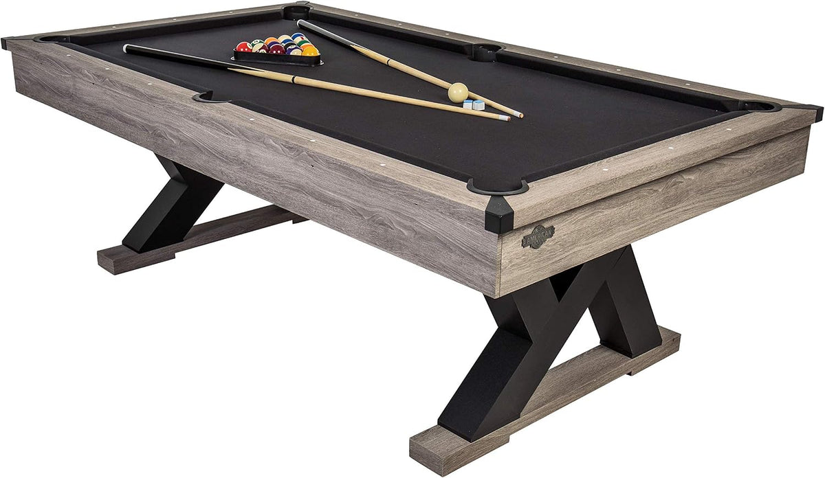 Grey farmhouse billiard table angled front-left view showing K-shaped legs and black playing surface with wooden cues.