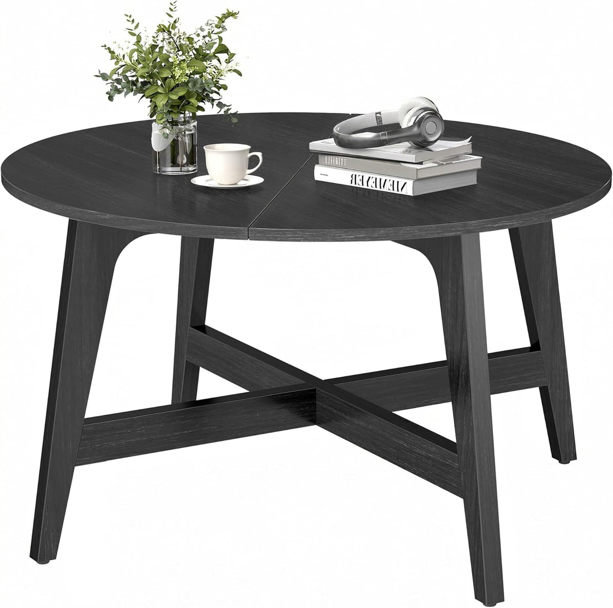 Black round coffee table on white background shown with books, headphones, and a small plant