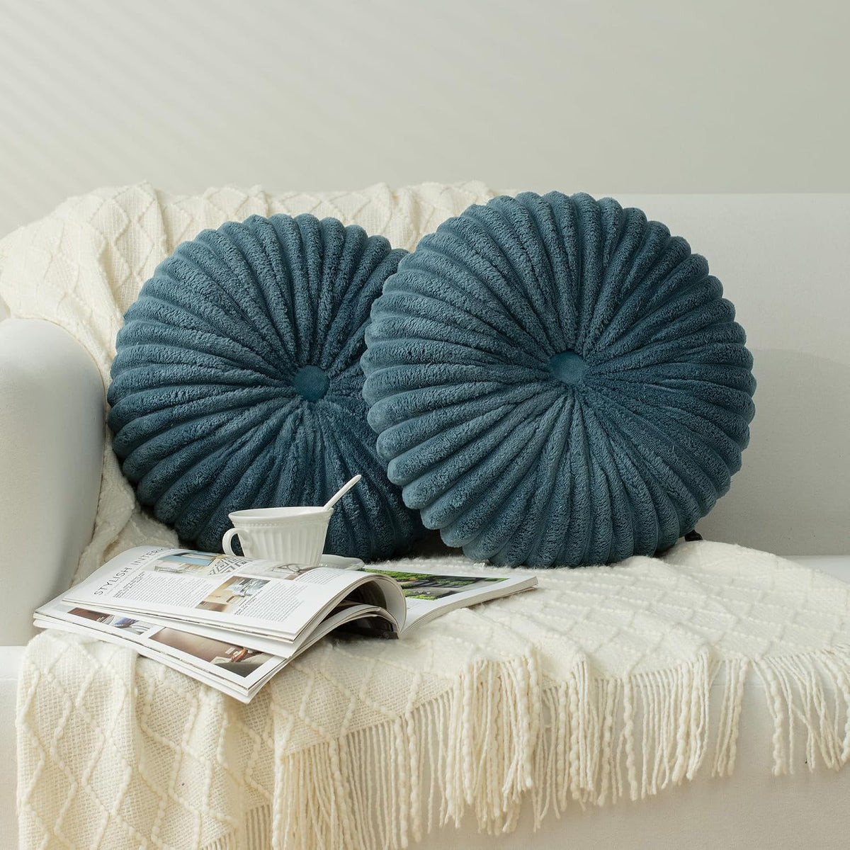 Pair of round textured teal pillows resting on a cream sofa with a blanket and magazine