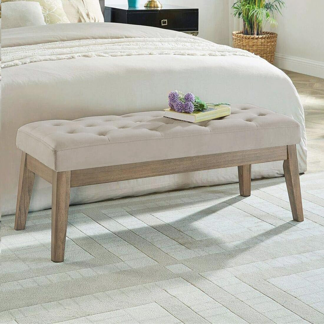 Light taupe velvet tufted bench placed at the foot of a bed in a softly lit bedroom