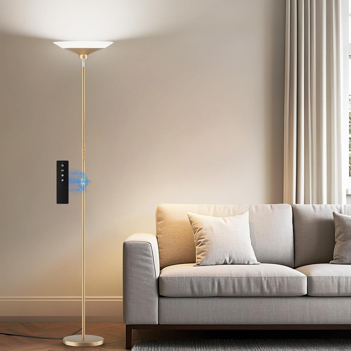 Gold-finish torchiere floor lamp beside a beige sofa, casting warm uplight on a blank wall.