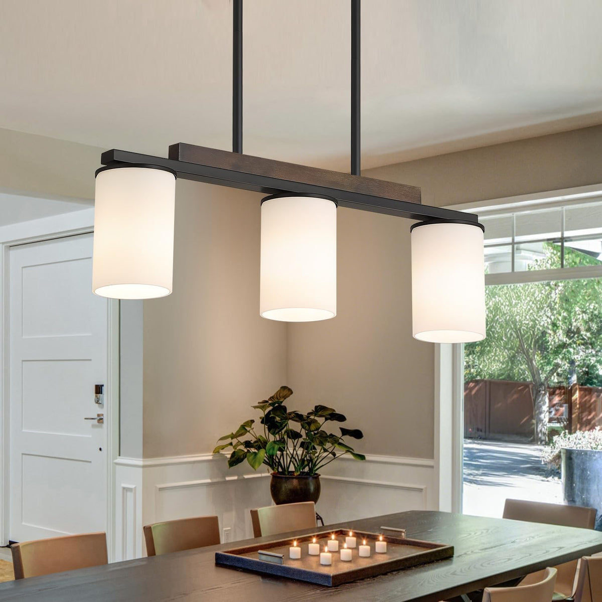 Three frosted cylindrical glass shades on a black linear chandelier above a dining table near a doorway.