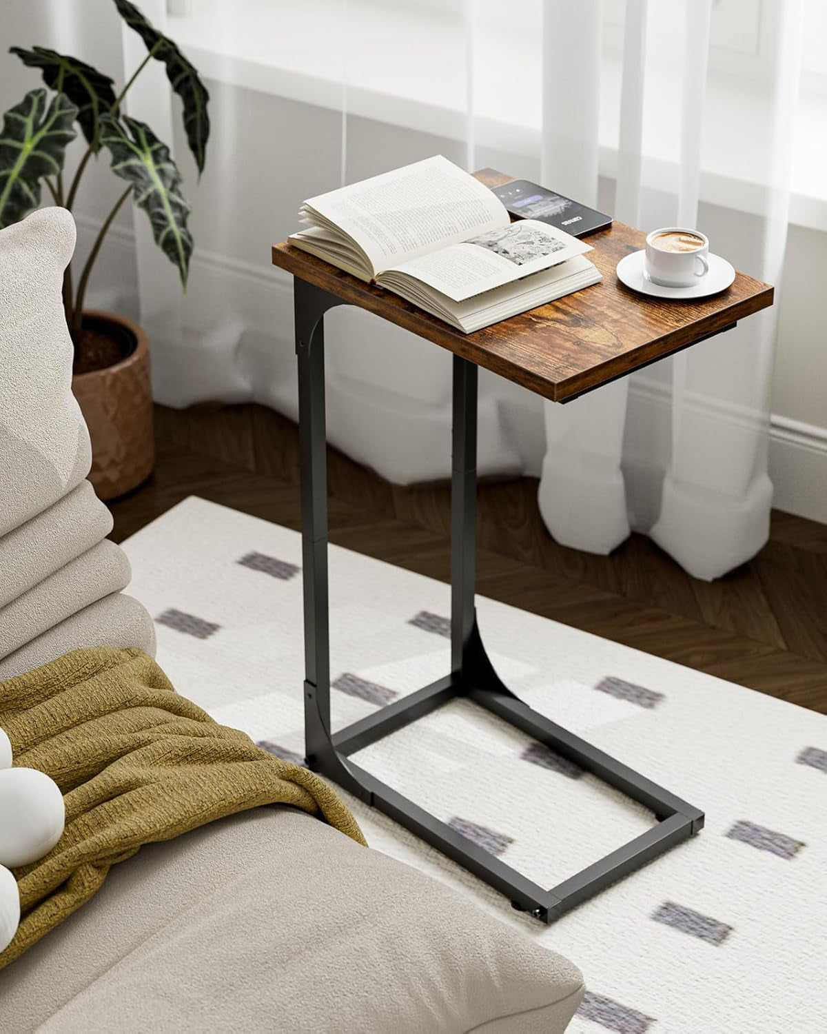 Single C-shaped side table with a rustic wood top beside a sofa, book and cup on top.
