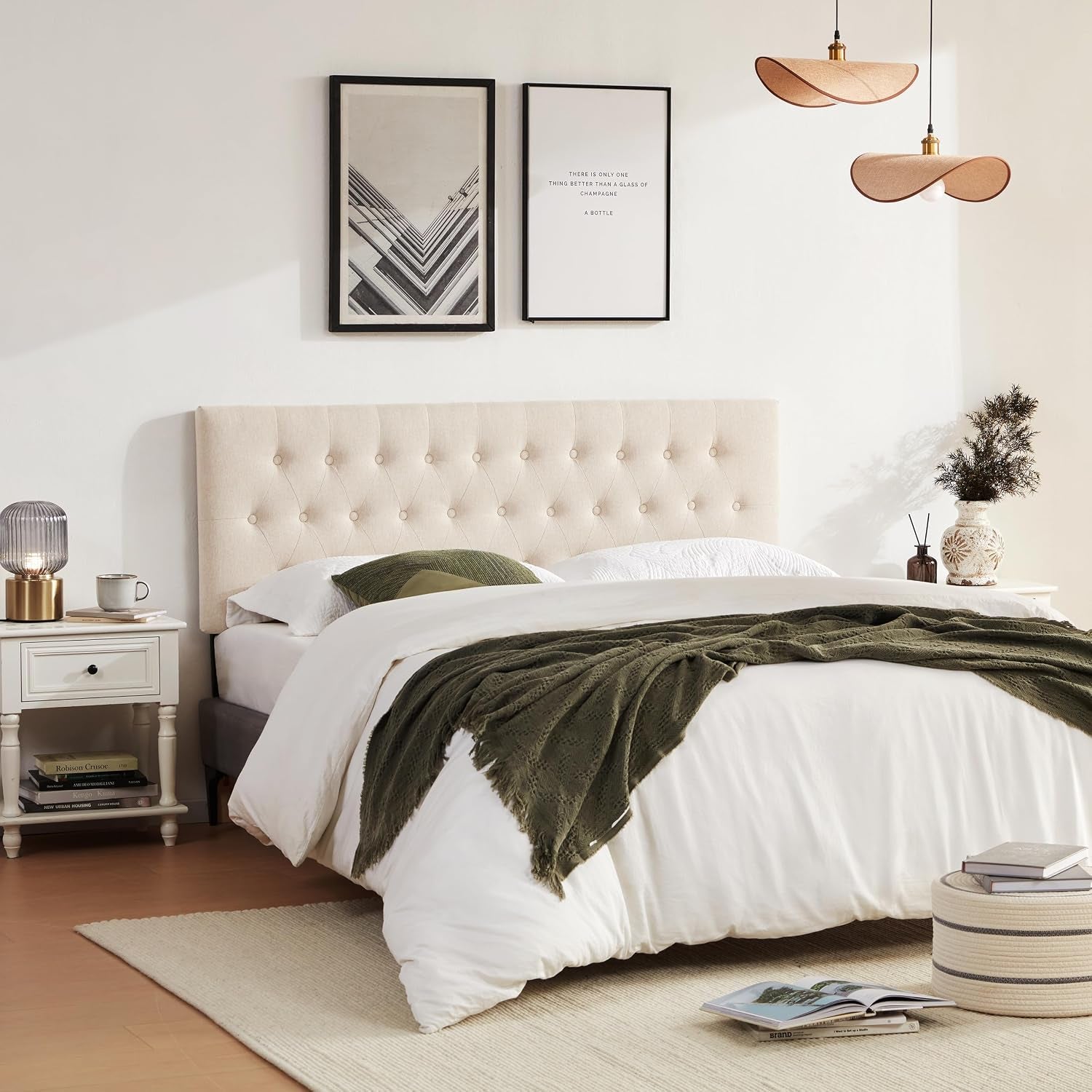 Beige tufted headboard in a full bedroom scene with nightstand, pendant lights and woven pouf.