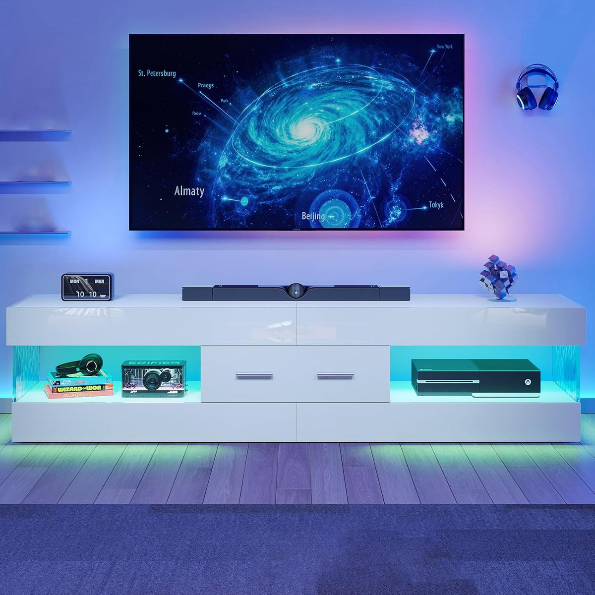 White TV stand front view with turquoise LED-lit shelves, center drawers and wall-mounted TV above