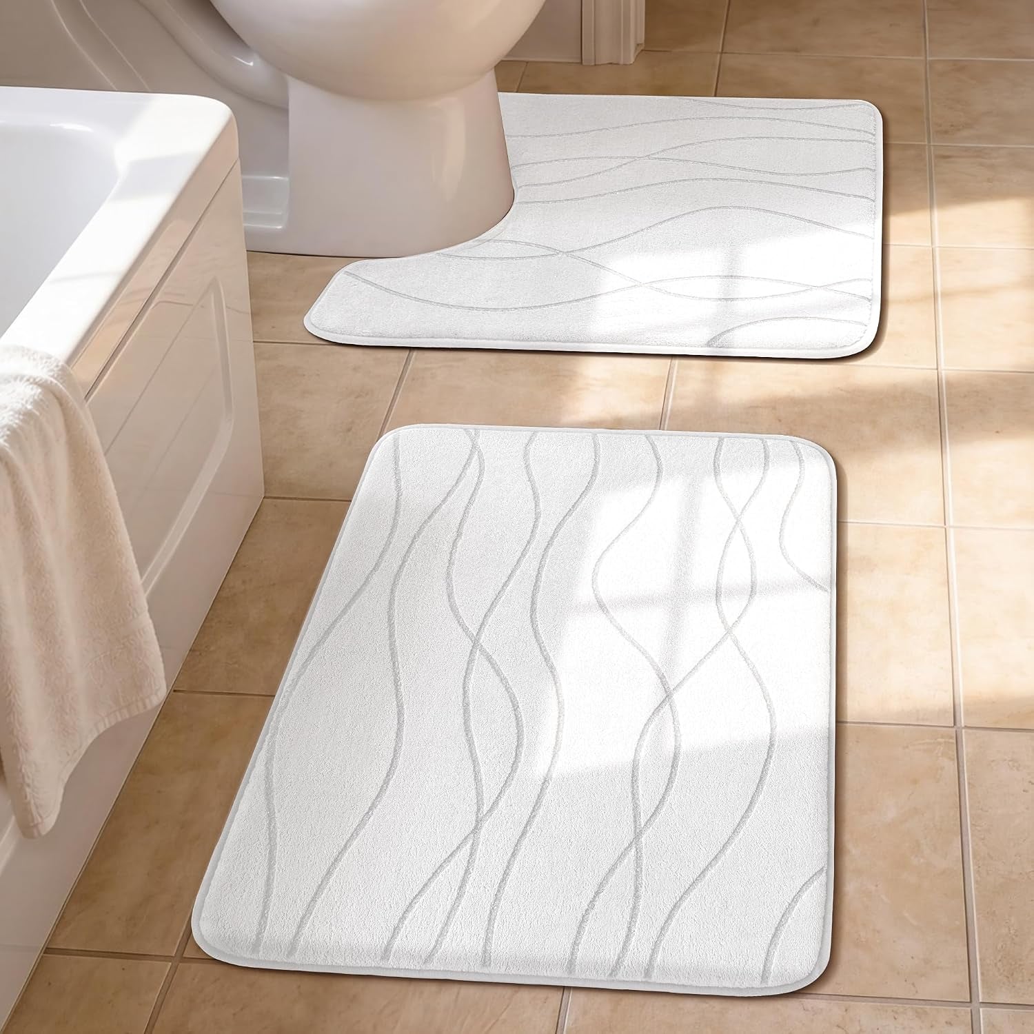 Two light-colored bath mats with wavy embossed pattern on tan tiled floor near tub and toilet