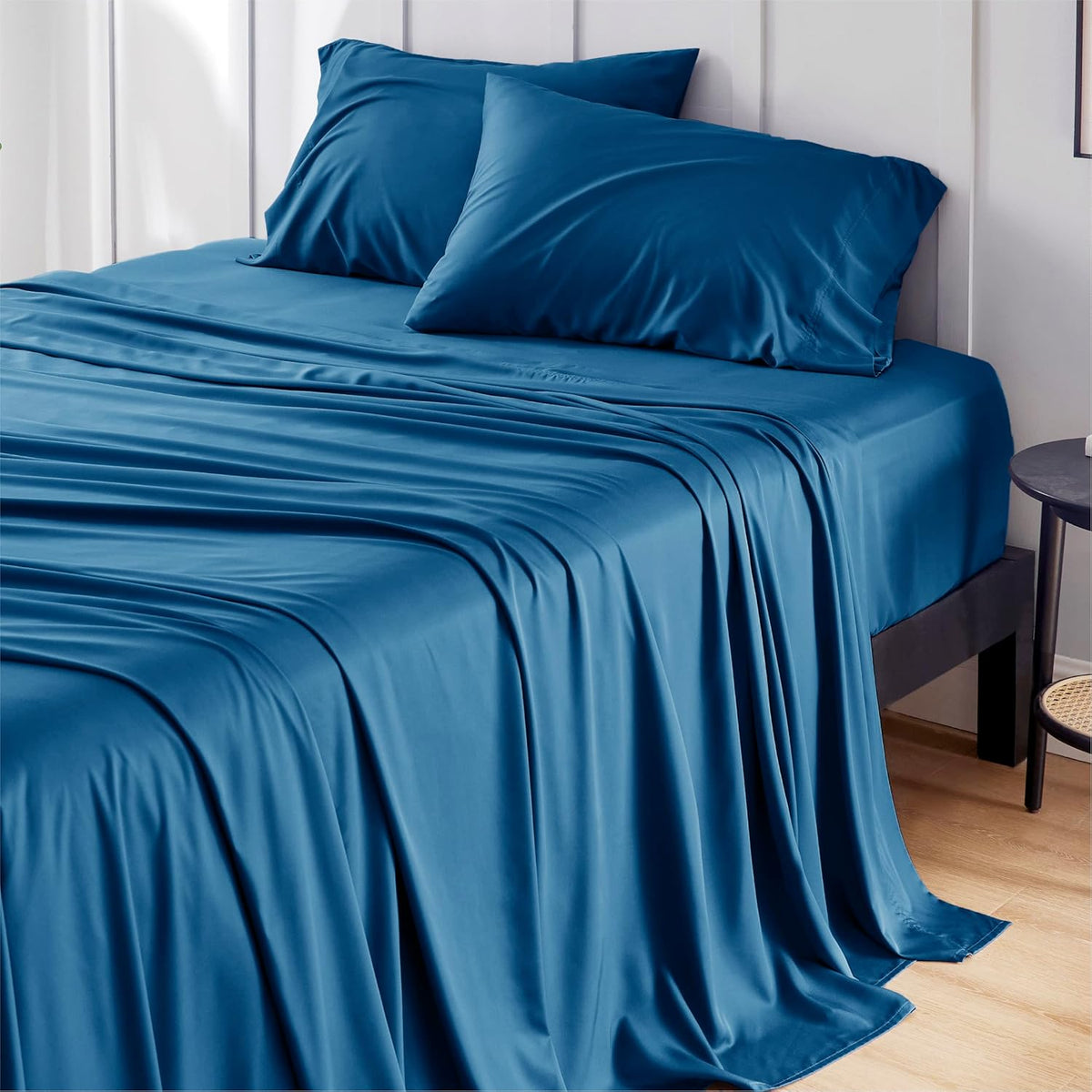 main room shot — deep teal sheets and two matching pillows with fabric draped to the floor beside a nightstand.