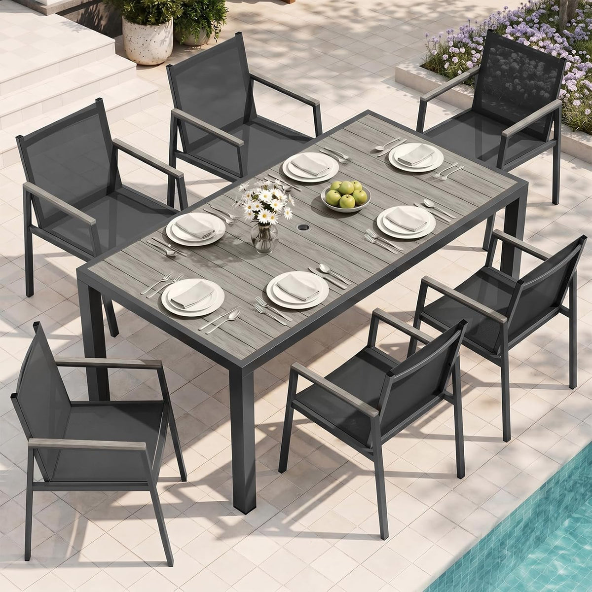 Rectangular outdoor dining table set by a pool with six dark-gray armchairs and place settings.