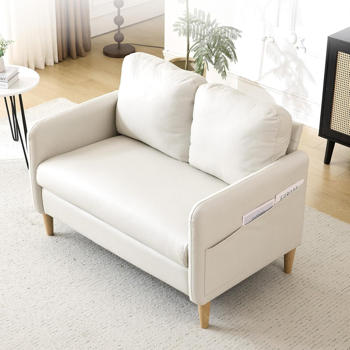Cream-colored loveseat shown at an angle with pocket on the arm holding magazines