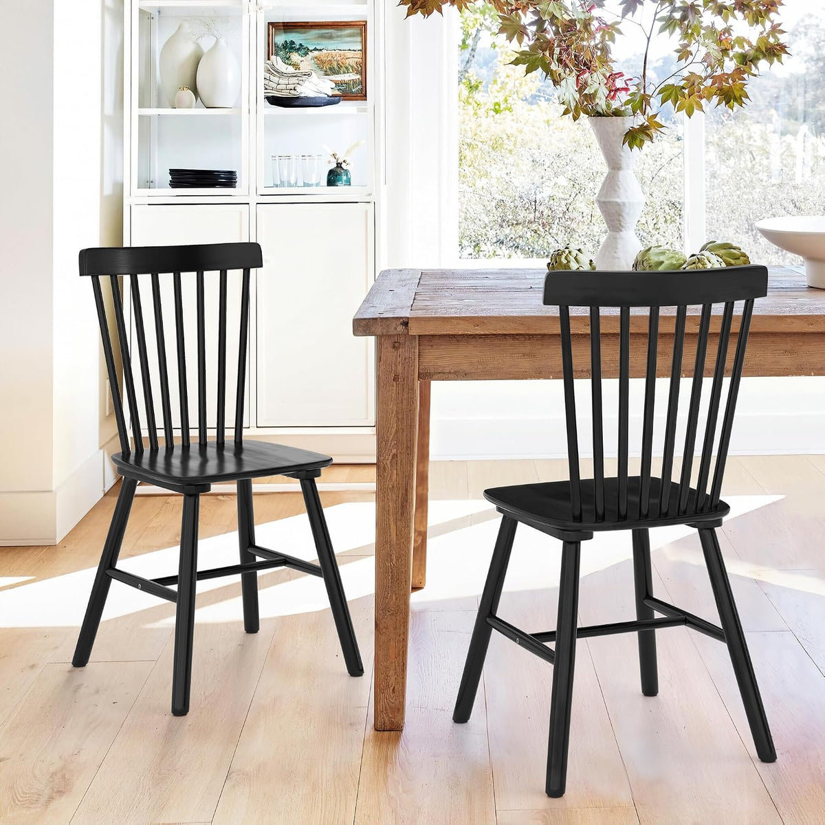 Two black spindle-back wooden dining chairs beside a rustic wood table in a bright dining room